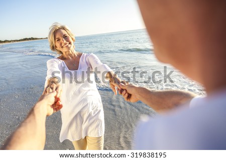 Happy senior man and woman couple walking or dancing and holding hands on a deserted tropical beach with bright clear blue sky
