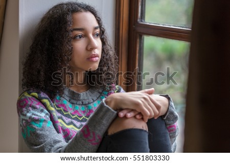 Beautiful mixed race African American girl teenager female young woman sad depressed or thoughtful looking out of a window