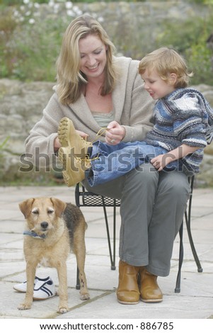 A young mother does up the bootlaces of her son while the family dog looks on