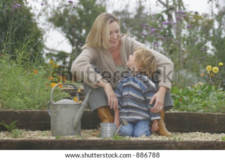 A young mother and her son in a flower filled garden with their watering cans