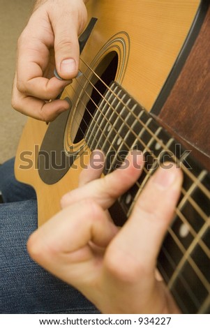 Shot of hands playing an acoustic guitar with a plectrum