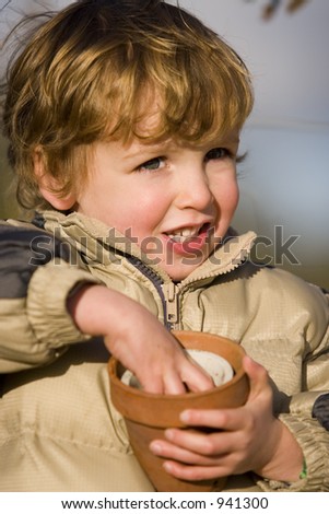 A young boy plays with two flower pots in a sunny garden