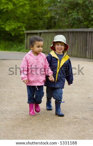 A little boy and girl wearing wellington boots holding hands and walking through a country park