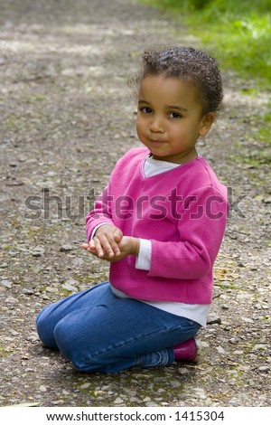 A beautiful mixed race girl outside kneeling down holding something secretly in her hands.