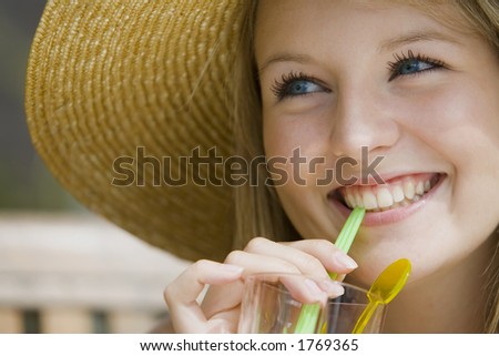 A beautiful young blond woman enjoying a tall drink  and wearing a big straw hat.