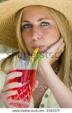 A beautiful young lady drinking a cocktail wearing a straw sun hat and bathed in summer sunshine