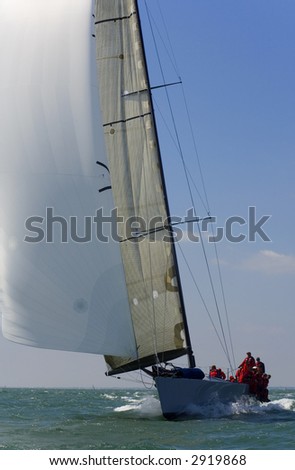 A fully crewed racing yacht with a white spinnaker catching the wind
