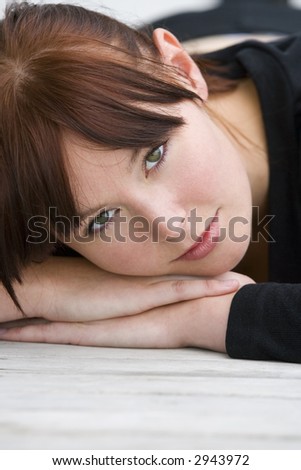 A beautiful young brunette woman laying down resting on her hands and looking enigmatically into the lens