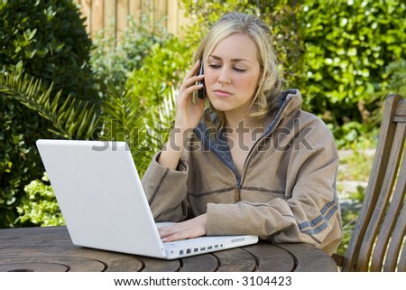 A beautiful young woman in the garden using a laptop and talking on a mobile phone