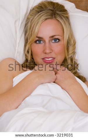 A beautiful young blond woman looking gorgeous in white bed sheets