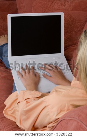 A young blond woman relaxing on a sette and using her white laptop, the screen is blank ready for any picture insertion.