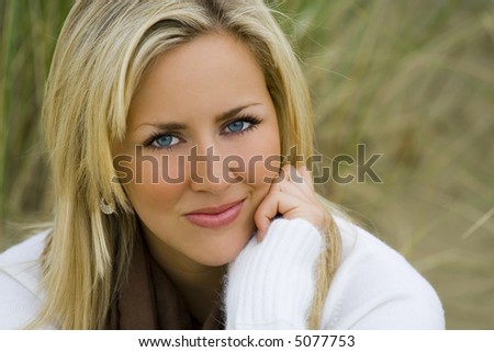 Close up portrait of a beautiful young blond woman with stunning blue eyes sitting amongst tall grass