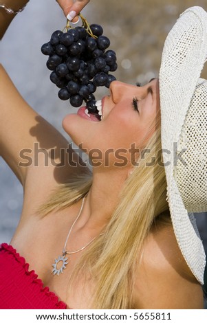 A beautiful young blond woman sitting in front of a fountain eating a bunch of black grapes