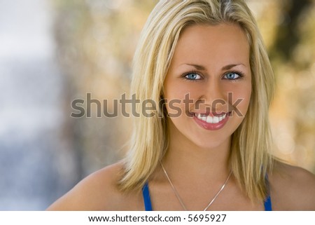Portrait of an absolutely gorgeous blond haired blue eyed woman bathed in diffused natural light and smiling in front of an out of focus waterfall