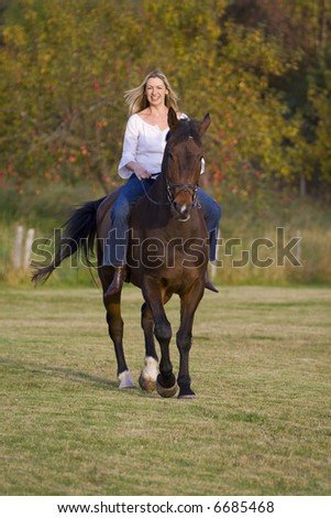An attractive young woman riding a horse bareback during the fall with an apple orchard in the background