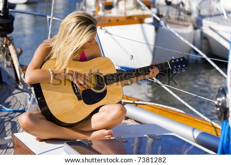 A beautiful young blond woman sitting on the deck of a boat playing her guitar