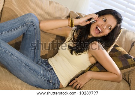 A beautiful young Hispanic woman laying on a settee and enjoying a call on her mobile phone
