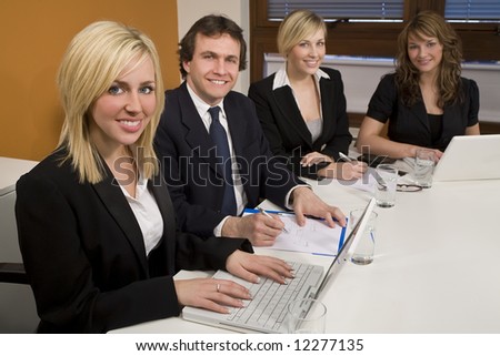 Three female executives and one male having a meeting in a boardroom - the focus is on the blond businesswoman in the foreground.
