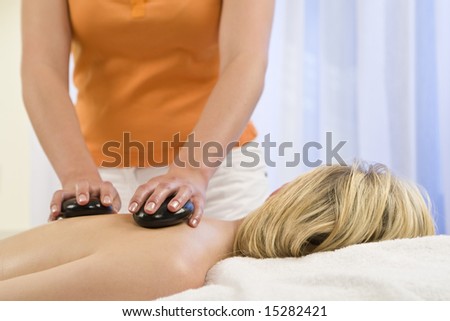 A beautiful young blond woman receives a hot stone massage from a beautician