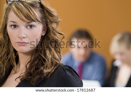 An attractive young female executive with her colleagues working on a laptop out of focus behind her