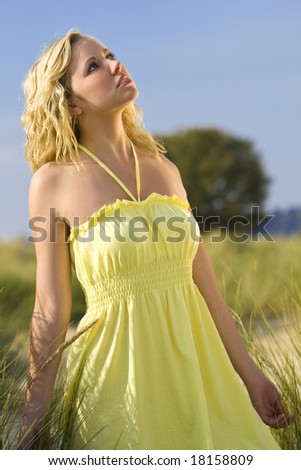 A beautiful blond young woman walking through tall grass illuminated by natural late evening golden sunshine and looking skywards