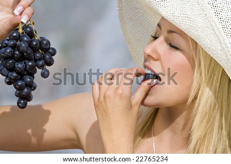 A beautiful young blond woman eating a bunch of black grapes