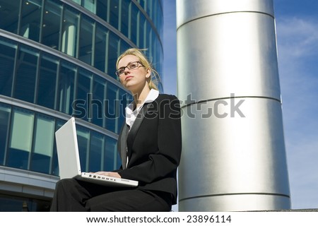A stunningly beautiful young woman working on her laptop outside in a hi-tech city environment