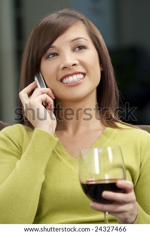 A beautiful young oriental woman with a wonderful toothy smile drinking red wine and chatting on her cell phone.