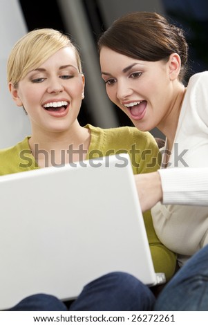 Two beautiful young women having fun on a white laptop computer