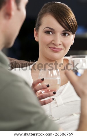 A beautiful brunette young woman drinking water and smiling while on a date with a young man who is out of focus in the foreground