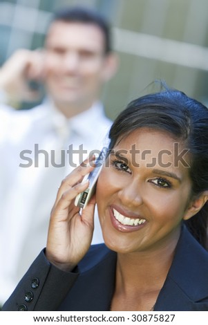 A beautiful young Asian businesswoman with a wonderful smile chatting on her cell phone with an out of focus male colleague behind her.