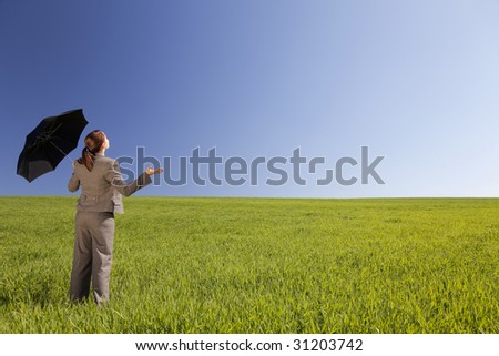Business concept shot of a beautiful young woman standing in a green field under a bright blue sky holding and umbrella and looking towards the light. Shot on location.
