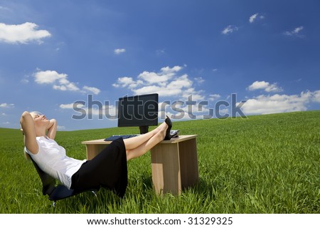 Business concept shot of a beautiful young woman relaxing at a desk in a green field with a bright blue sky. Shot on location.