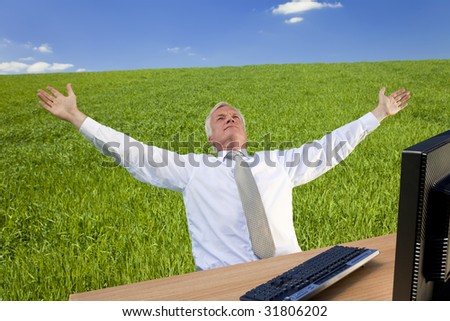 Business concept shot showing an older male executive using a computer in a green field with a blue sky complete with fluffy white clouds. Shot on location not in a studio.