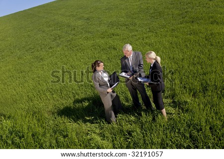 High angle concept shot of a team of three people one man and two women in a green field with a bright blue sky discussing plans. Shot on location.