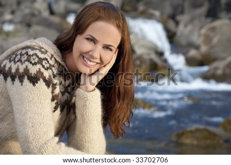 A beautiful Scandinavian woman wearing traditionally patterned knitwear sitting and relaxing by a flowing mountain stream