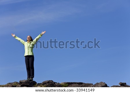 A beautiful young woman stands on the horizon arms raised celebrating reaching the top of a mountain.