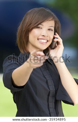 A beautiful young oriental woman with a wonderful smile chatting on her smart cell phone.