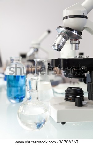 A microscope in a laboratory environment with various flasks and equipment