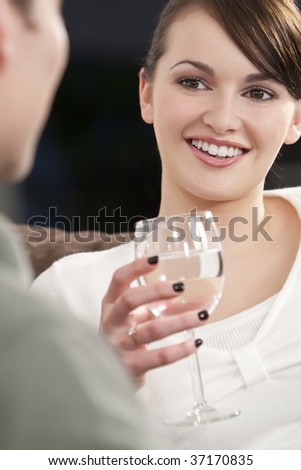 A beautiful brown eyed brunette young woman drinking water and smiling while on a date with a young man who is out of focus in the foreground
