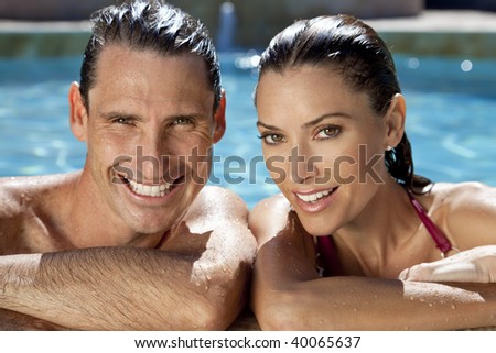 Close up portrait of a beautiful happy man and woman couple resting on their hands at the side of a sun bathed swimming pool smiling with perfect teeth.