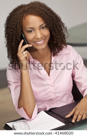 A beautiful mixed race African American girl, possibly a student or businesswoman sitting at a desk talking on her cell phone.