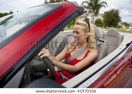 A beautiful young blond woman driving her convertible car wearing a red dress and sunglasses