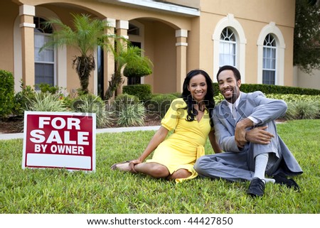 A happy African American man and woman couple outside a large house with a For Sale sign
