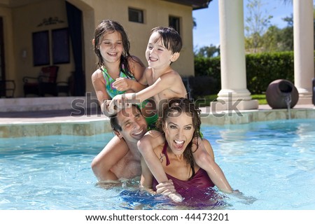 A mother and father having fun on vacation playing with their children on their shoulders in a swimming pool