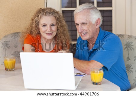 A senior retired man and woman couple sitting outside using a wireless laptop computer to surf the internet.