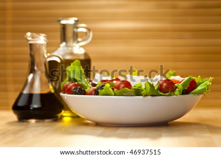 Tomato, mozzarella, or feta cheese salad with black olives, olive oil and balsamic vinegar dressing in bottles out of focus in the background, shot in golden sunshine