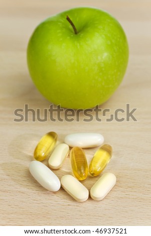 A green apple and tablets either medicinal pills or nutritional vitamin supplements. The focus is on the capsules pills and tablets in the foreground.
