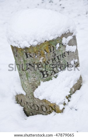 A vintage stone carved British milestone road sign covered in winter snow and showing distances to London, Reading, Newbury and Bath