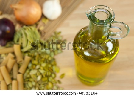 A bottle of extra virgin olive oil with dried pasta, red onions, white onions and garlic cloves out of focus in the background
